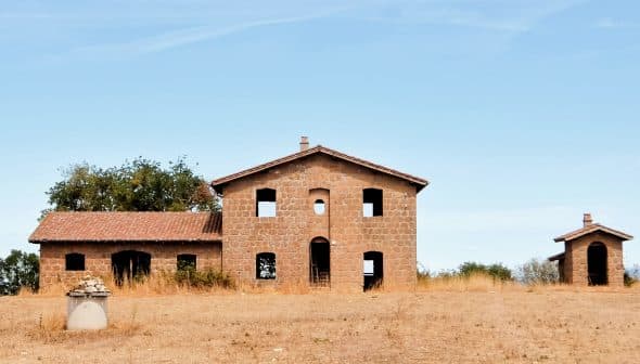Abandoned stone building with multiple windows and a roof, set against a clear sky. - Olive Oil Times