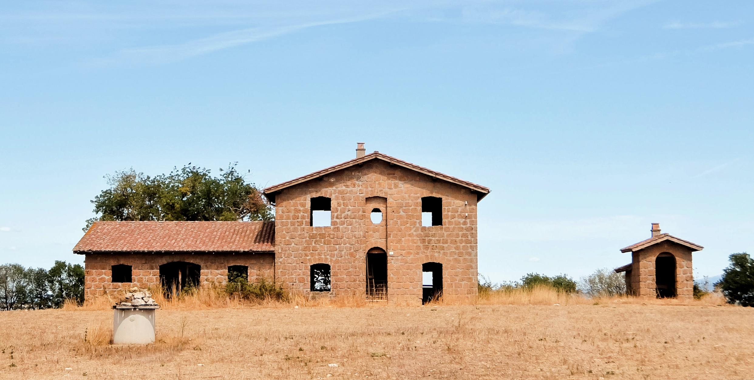 Abandoned stone building with multiple windows and a roof, set against a clear sky. - Olive Oil Times
