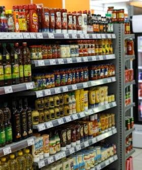 A grocery store aisle displaying various bottles of condiments and cooking oils on shelves. - Olive Oil Times