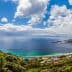 Panoramic view of a coastal landscape featuring a beach, ocean, and distant mountains under a cloudy sky. - Olive Oil Times