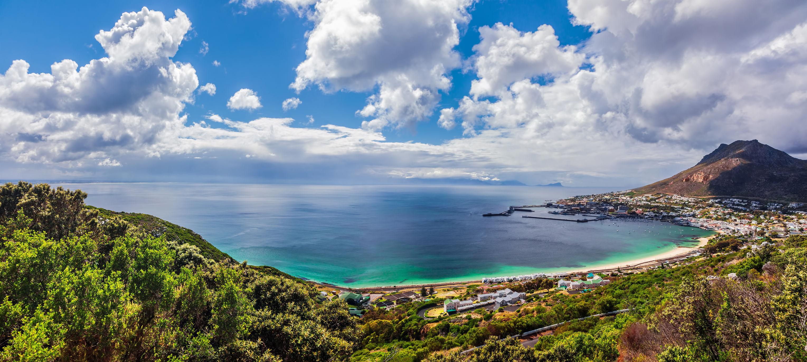 Panoramic view of a coastal landscape featuring a beach, ocean, and distant mountains under a cloudy sky. - Olive Oil Times
