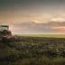 Red tractor plowing a field during sunset with a cloudy sky in the background. - Olive Oil Times