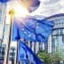 European Union flags waving in front of a modern building with glass architecture. - Olive Oil Times