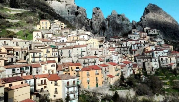 A hillside village featuring colorful houses with red roofs against rocky mountains. - Olive Oil Times