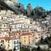 A hillside village featuring colorful houses with red roofs against rocky mountains. - Olive Oil Times