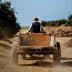 A farmer wearing a hat driving a wooden cart along a dirt path surrounded by vegetation. - Olive Oil Times
