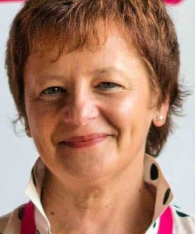 Woman with short brown hair wearing a polka dot blouse and smiling at the camera. - Olive Oil Times