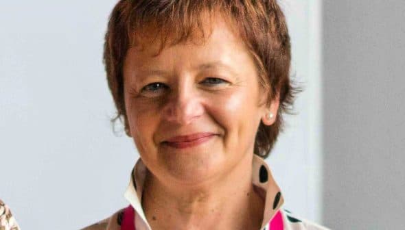 Woman with short brown hair wearing a polka dot blouse and smiling at the camera. - Olive Oil Times