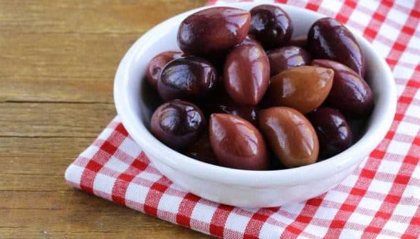 A bowl filled with various types of olives on a red and white checkered cloth. - Olive Oil Times