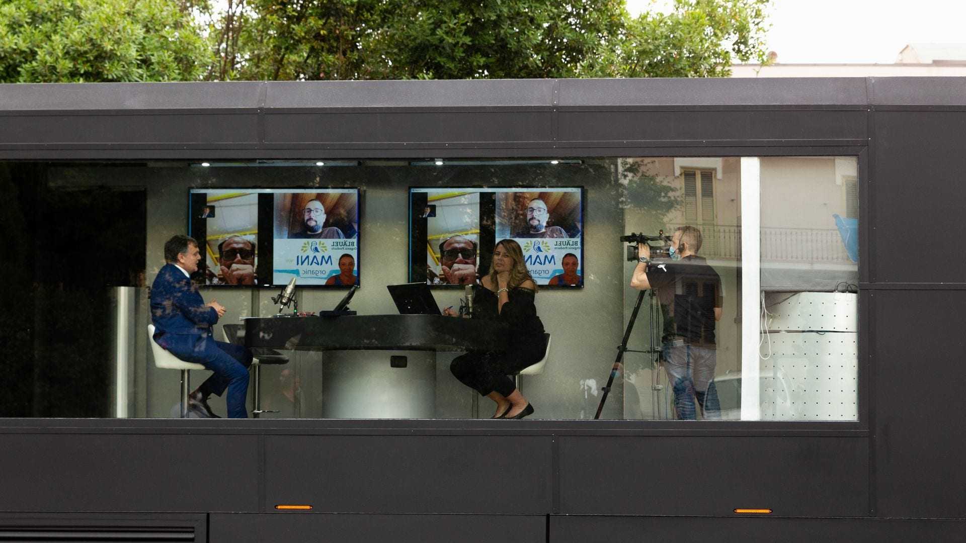 Two individuals participating in a video conference with screens displaying images in a modern setting. - Olive Oil Times