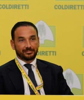 Man wearing a suit and tie sitting at a table with a Coldiretti banner in the background. - Olive Oil Times