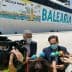 Two men speaking during a press conference in front of a Balearia ferry with promotional graphics. - Olive Oil Times