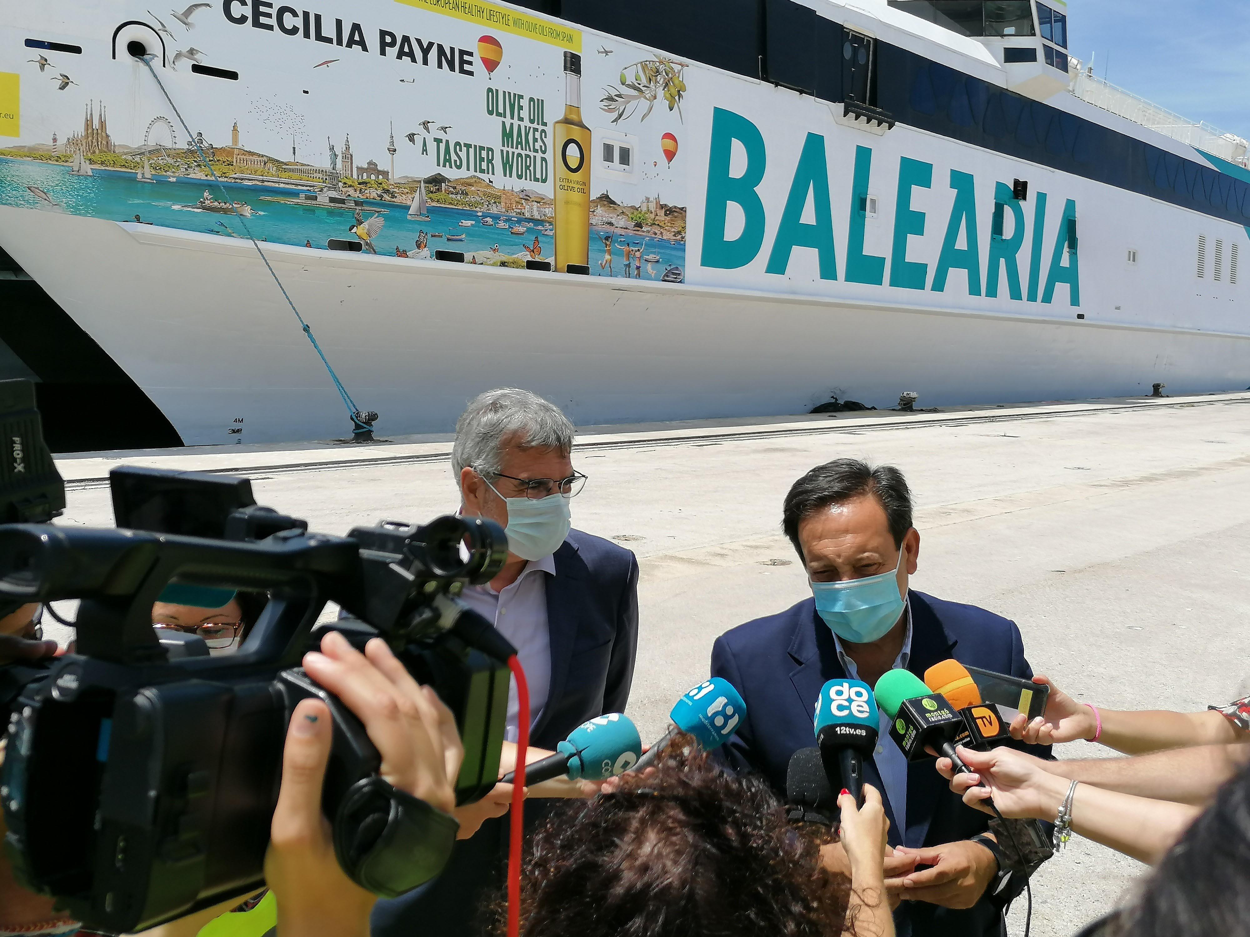 Two men speaking during a press conference in front of a Balearia ferry with promotional graphics. - Olive Oil Times
