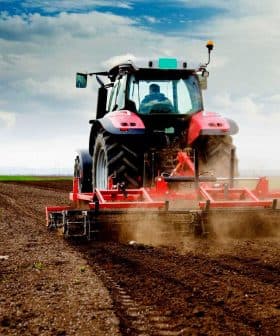 Red tractor working on a field, tilling the soil with dust being kicked up. - Olive Oil Times