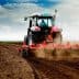 Red tractor working on a field, tilling the soil with dust being kicked up. - Olive Oil Times