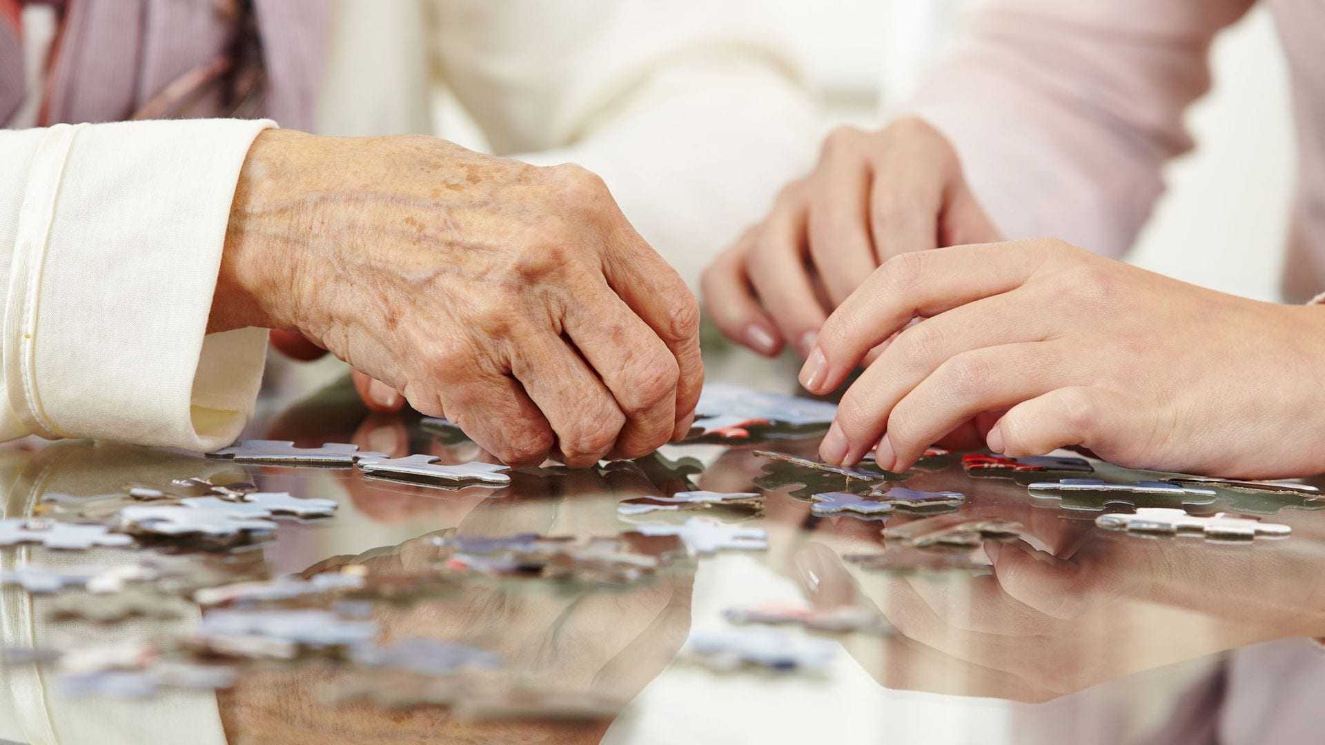 Two hands working together to assemble pieces of a jigsaw puzzle on a table. - Olive Oil Times