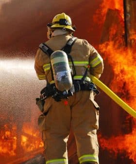 Firefighter in protective gear using a hose to extinguish flames from a burning structure. - Olive Oil Times