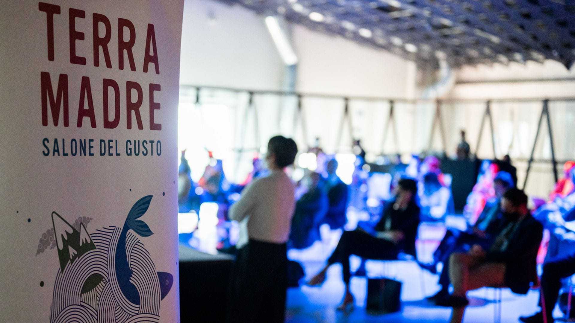Banner for Terra Madre Salone del Gusto event with audience in the background. - Olive Oil Times