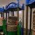 Four traditional oil press machines with stacked materials and pressure gauges in a processing facility. - Olive Oil Times
