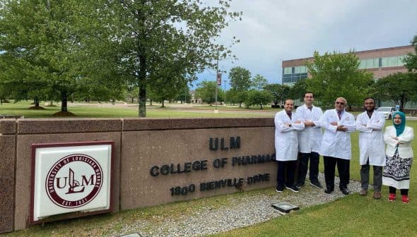 Group of five individuals in white lab coats standing in front of ULM College of Pharmacy sign. - Olive Oil Times