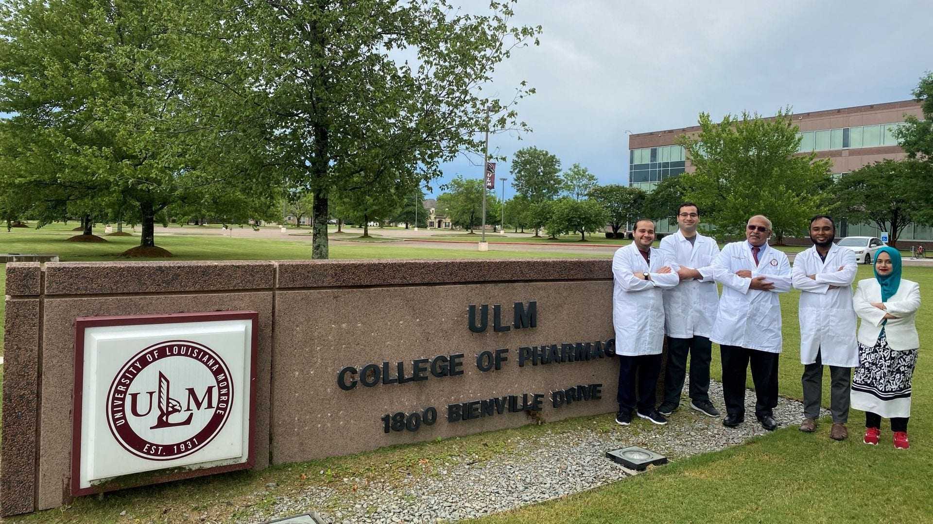 Group of five individuals in white lab coats standing in front of ULM College of Pharmacy sign. - Olive Oil Times