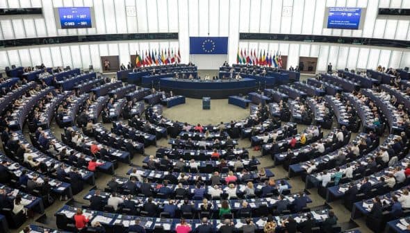 Interior view of the European Parliament in session with members seated in a circular arrangement. - Olive Oil Times