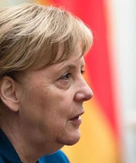 Profile view of Angela Merkel with short hair and a blue jacket, set against a blurred background. - Olive Oil Times