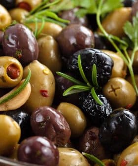 A bowl of assorted green and black olives with herbs and spices. - Olive Oil Times