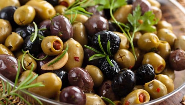 A bowl of assorted green and black olives with herbs and spices. - Olive Oil Times