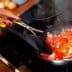 Person stirring a mixture of chopped tomatoes and bacon in a frying pan on a stovetop. - Olive Oil Times