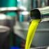 Stream of bright yellow olive oil pouring from a metal spout into a container. - Olive Oil Times