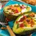 Baked avocado halves filled with egg, topped with bacon bits and chives on a blue plate. - Olive Oil Times