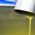 Stream of fresh olive oil pouring from a metal spout into a container during production. - Olive Oil Times