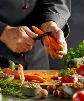 Chef peeling a carrot with various vegetables and herbs on a kitchen counter. - Olive Oil Times