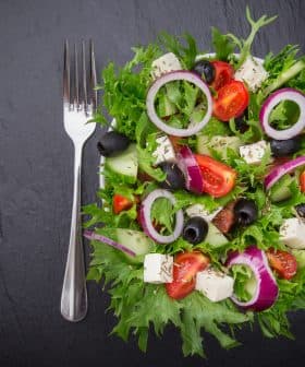 A colorful garden salad featuring mixed greens, tomatoes, cucumbers, olives, and feta cheese on a dark surface. - Olive Oil Times