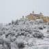 A snow-covered village with buildings and trees blanketed in white snow on a hillside. - Olive Oil Times