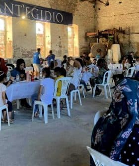 People seated at tables during a community gathering at SantEgidio with food and drinks. - Olive Oil Times