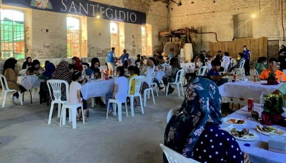 People seated at tables during a community gathering at SantEgidio with food and drinks. - Olive Oil Times