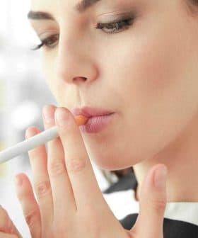 A woman with long hair lighting a cigarette with a lighter in her hand. - Olive Oil Times