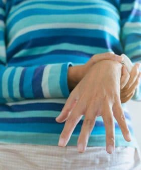 Individual wearing a striped sweater, holding their wrist with one hand while standing indoors. - Olive Oil Times