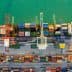 Aerial view of a cargo ship docked at a port with cranes and stacked containers. - Olive Oil Times