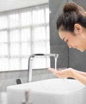 A woman in a white robe washing her hands at a modern sink with flowing water. - Olive Oil Times