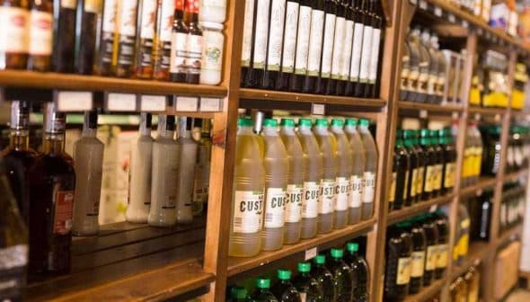 Shelves displaying various bottles of oils and condiments in a store. - Olive Oil Times