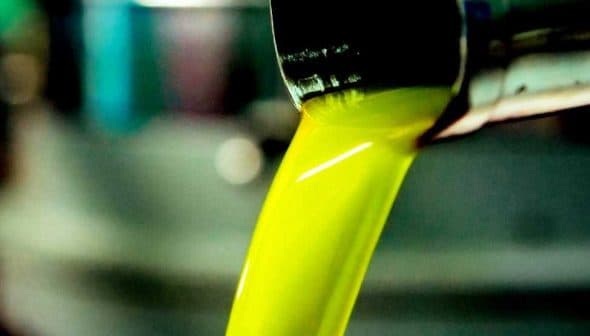 Stream of bright green olive oil pouring from a metal spout into a container. - Olive Oil Times