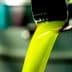 Stream of bright green olive oil pouring from a metal spout into a container. - Olive Oil Times