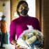 A woman wearing a pink sweater and black mask holds a bag of food items in a corridor. - Olive Oil Times