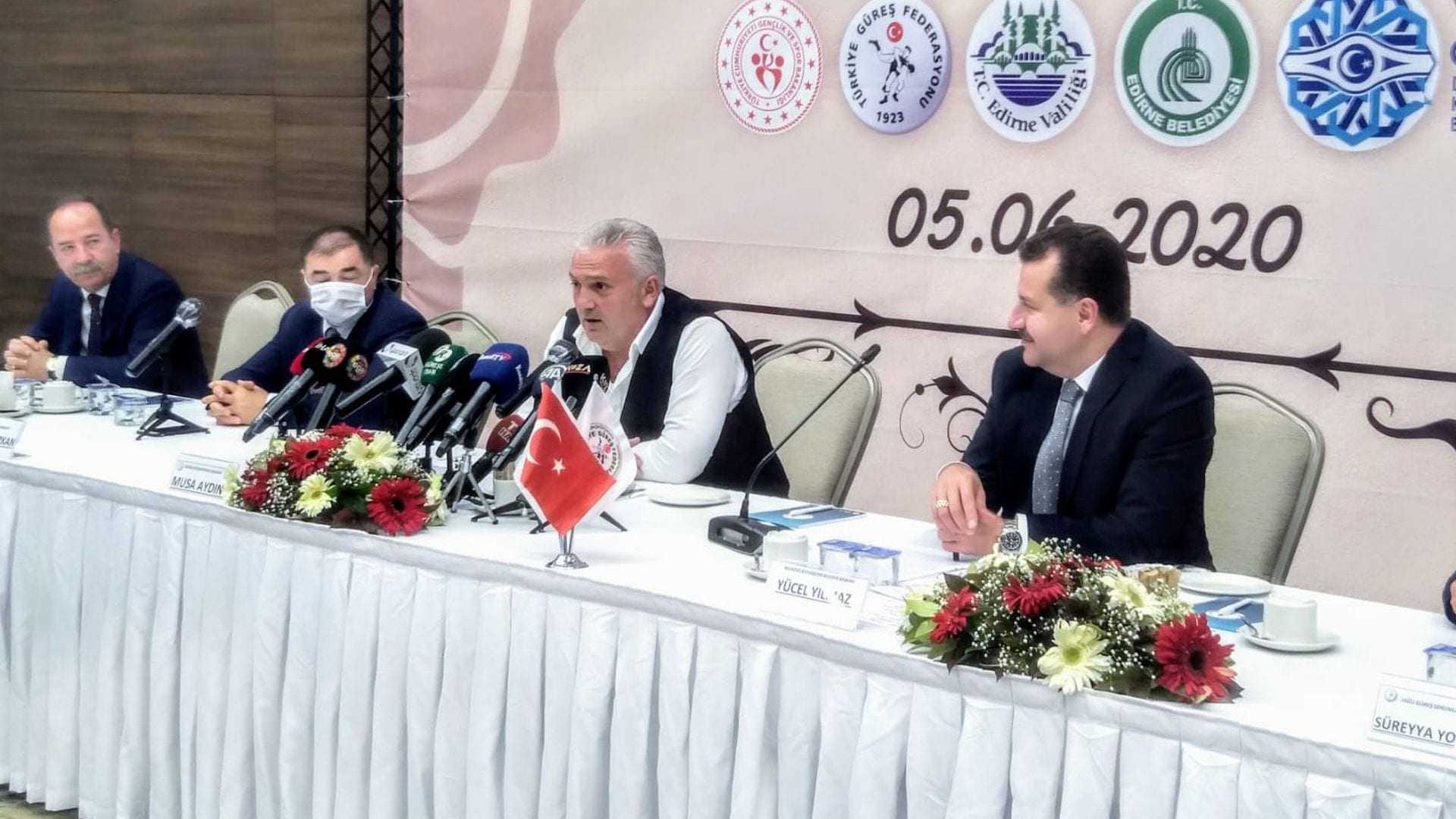 Group of officials seated at a table during a press conference with microphones and a Turkish flag. - Olive Oil Times
