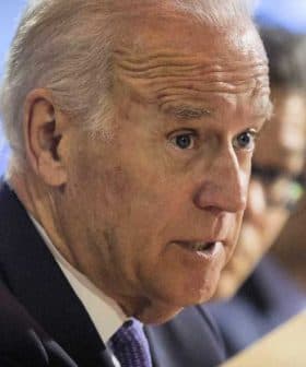 A man in a suit speaking during a conference, holding a document in his hand. - Olive Oil Times