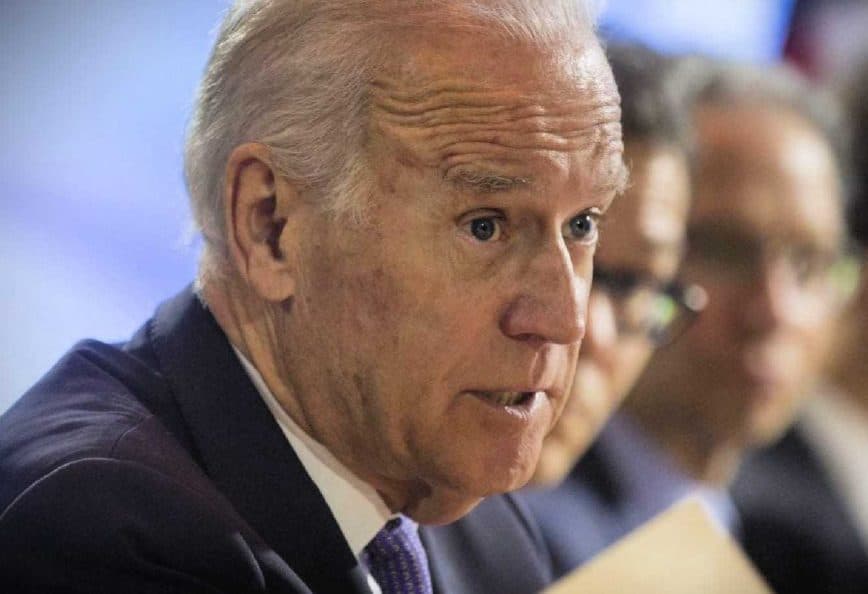 A man in a suit speaking during a conference, holding a document in his hand. - Olive Oil Times