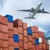 An airplane flying above a stack of colorful shipping containers at a port. - Olive Oil Times